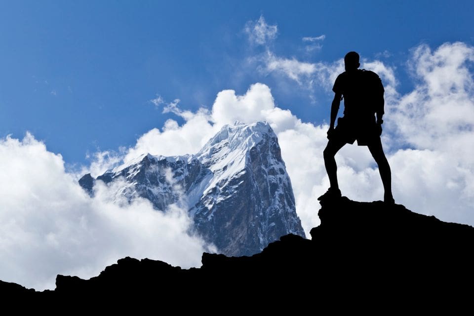 A man standing on top of a mountain with clouds in the background.