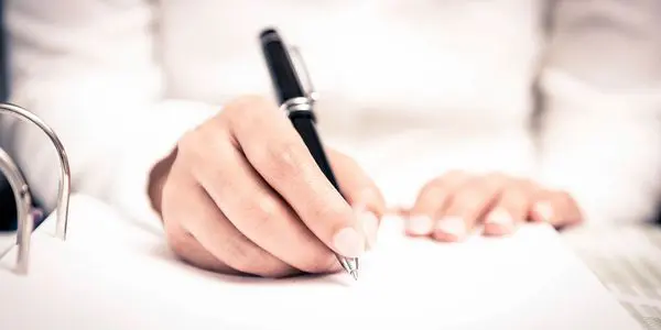 A person writing on paper with a pen.